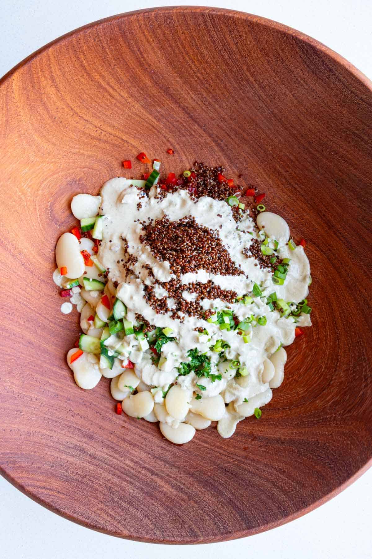Butter beans, red quinoa, olives, cucumber, chopped herbs, scallions, and bell pepper with pumpkin seed dressing in a bowl.