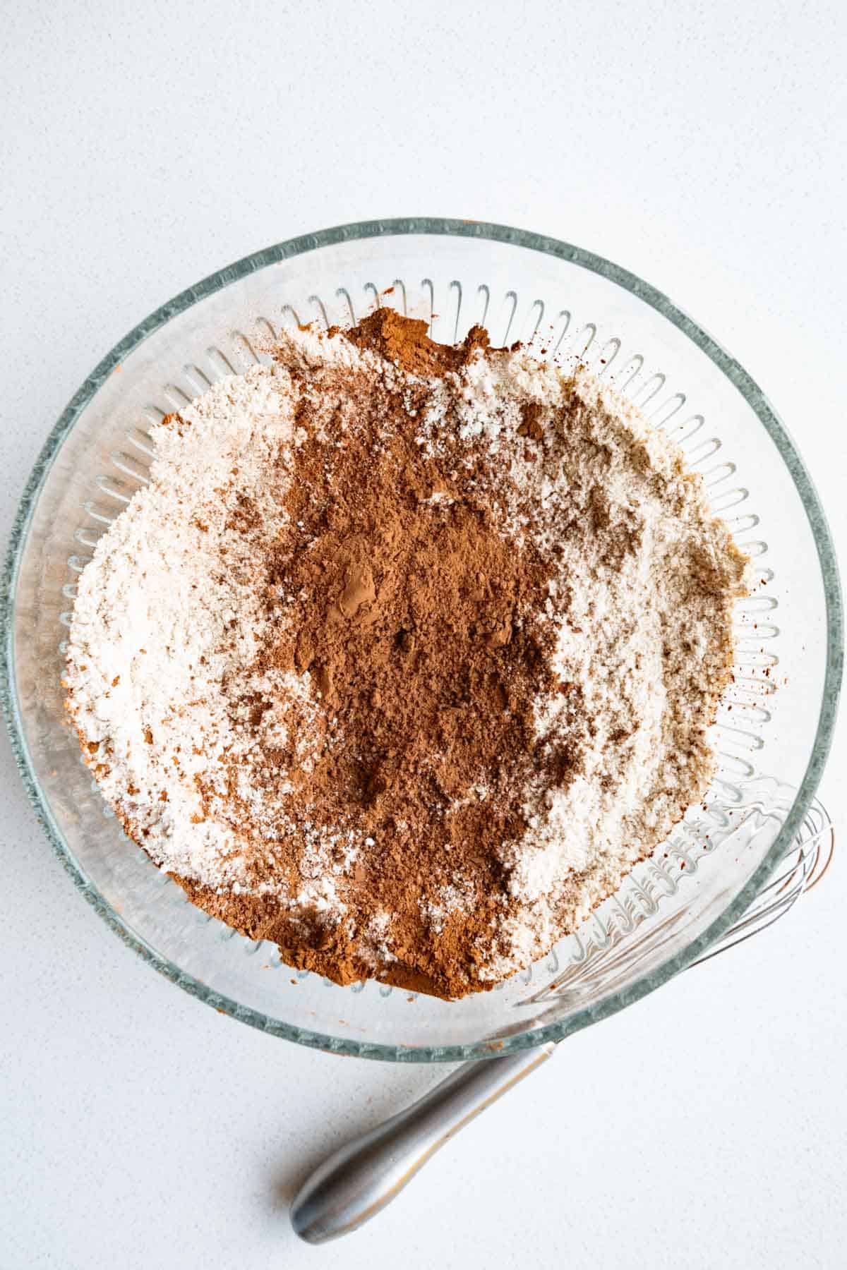 Oat flour, sorghum flour, cocoa powder, baking soda, and baking powder with a whisk in a bowl.