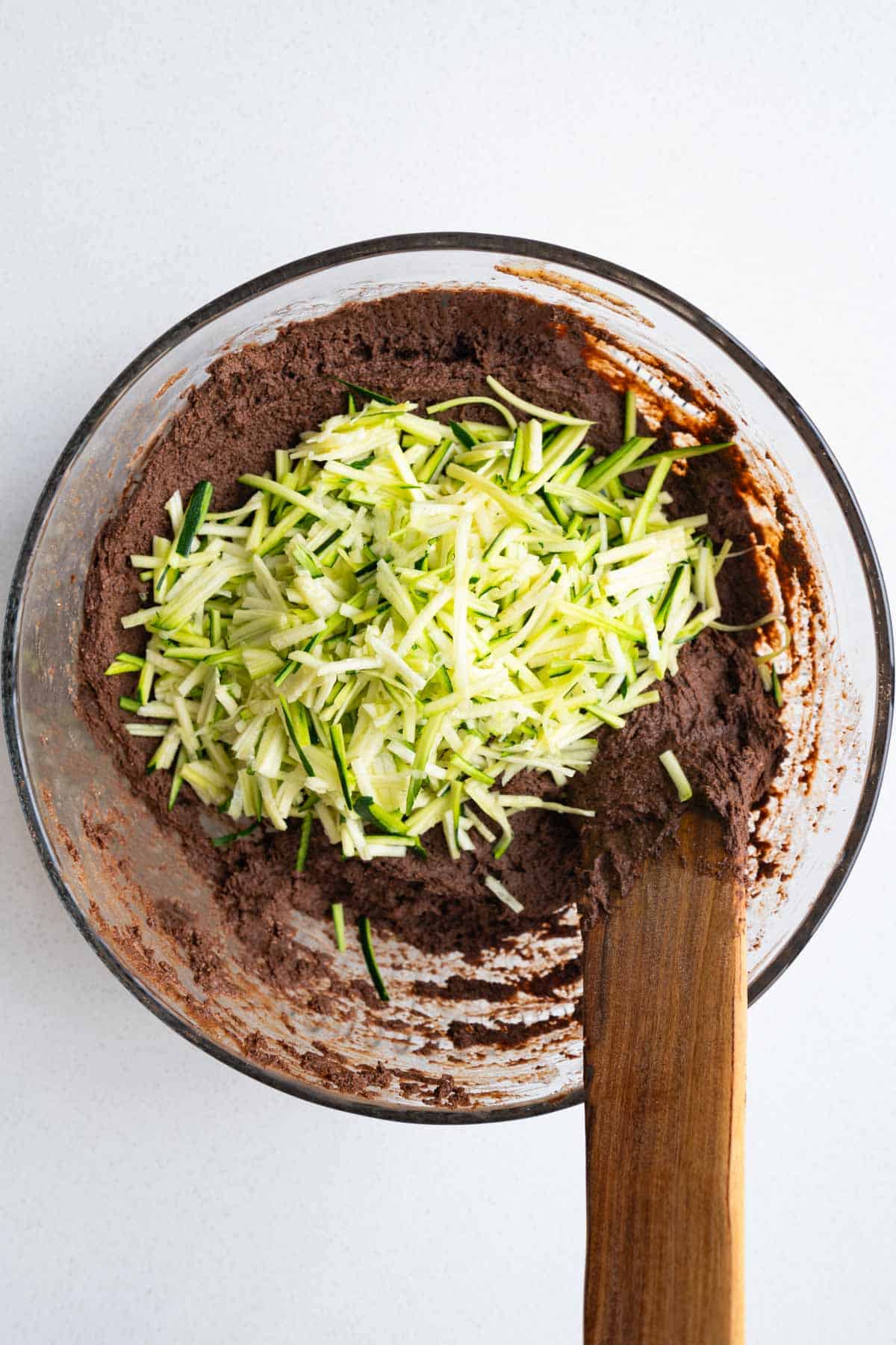 Chocolate batter in a glass bowl with grated zucchini.