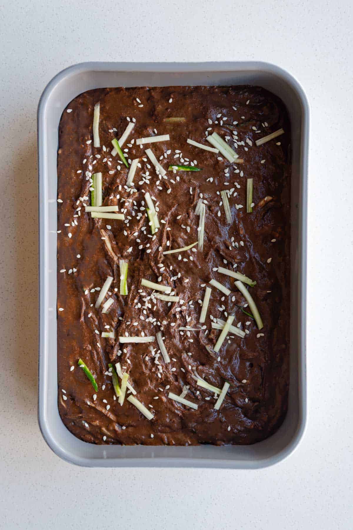 Healthy chocolate cake batter with zucchini and sesame seeds in a baking dish.