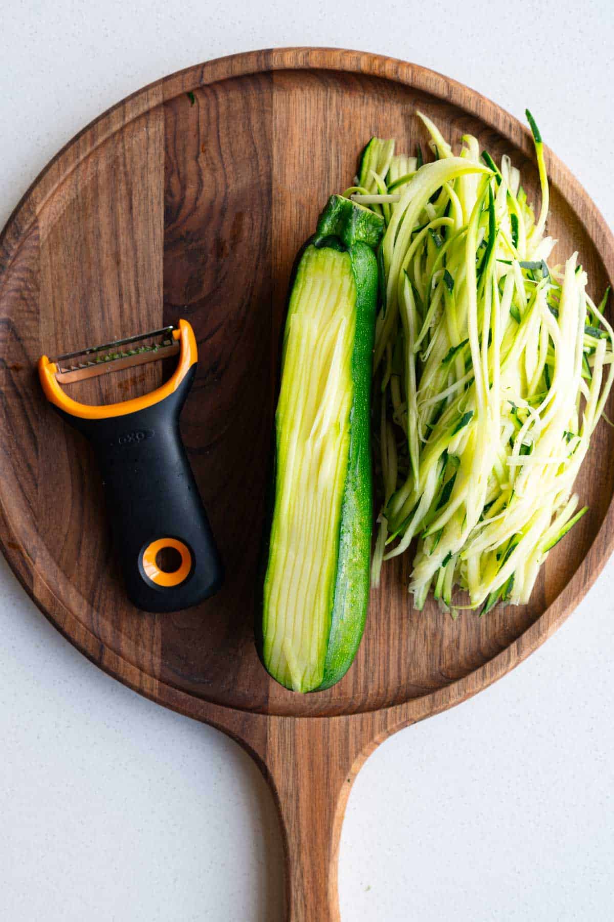 Julienned zucchini using a grater on a wooden cutting board.