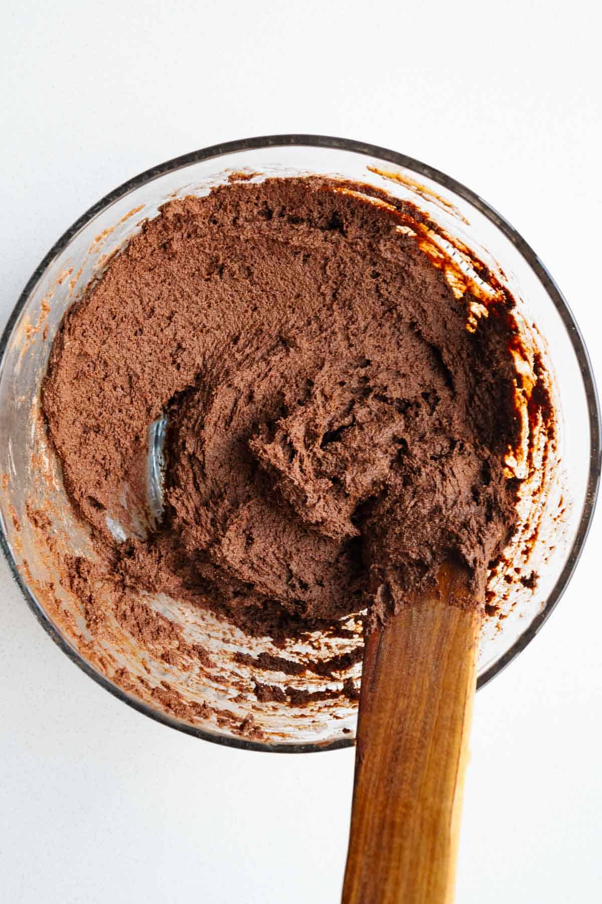 Chocolate cake batter in a glass bowl with a wooden spatula.