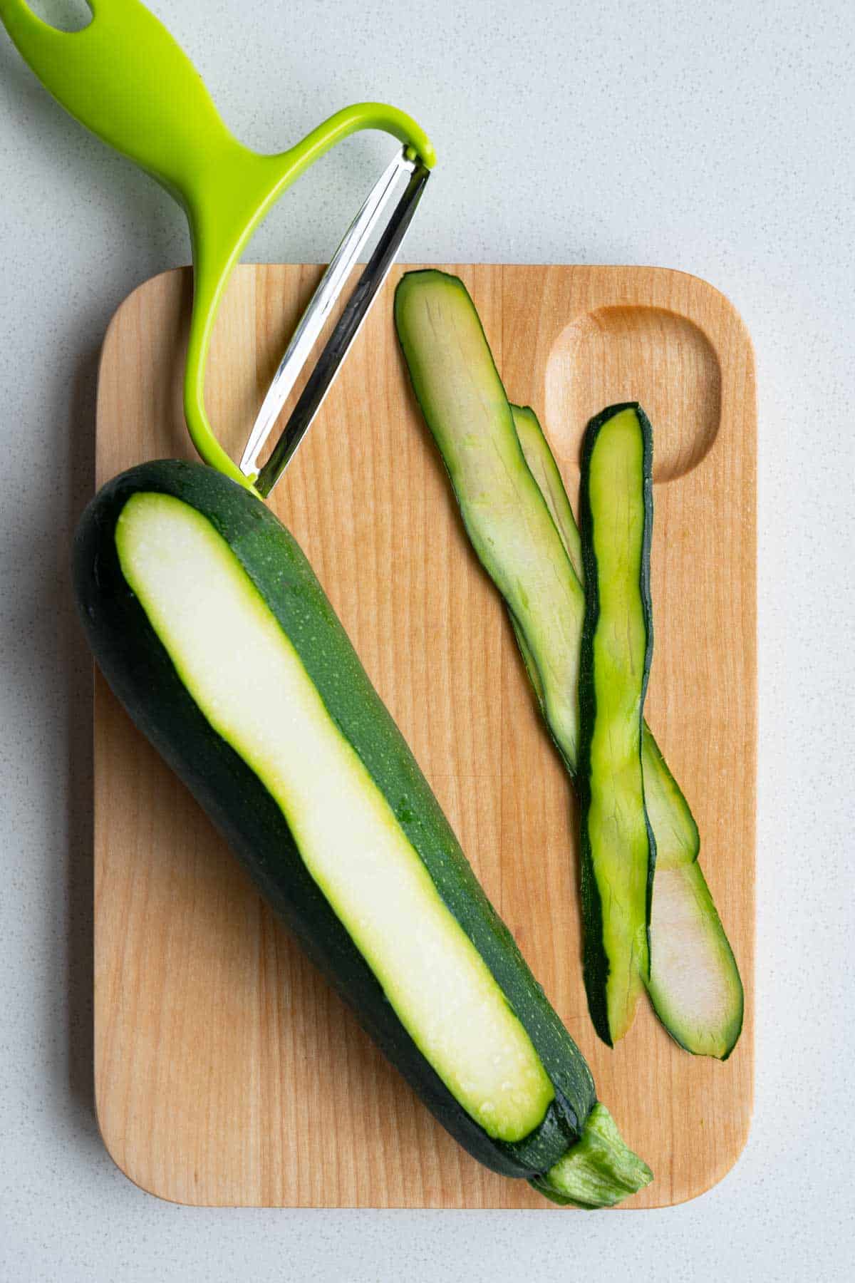 Thinly sliced zucchini with a Y peeler on a cutting board.