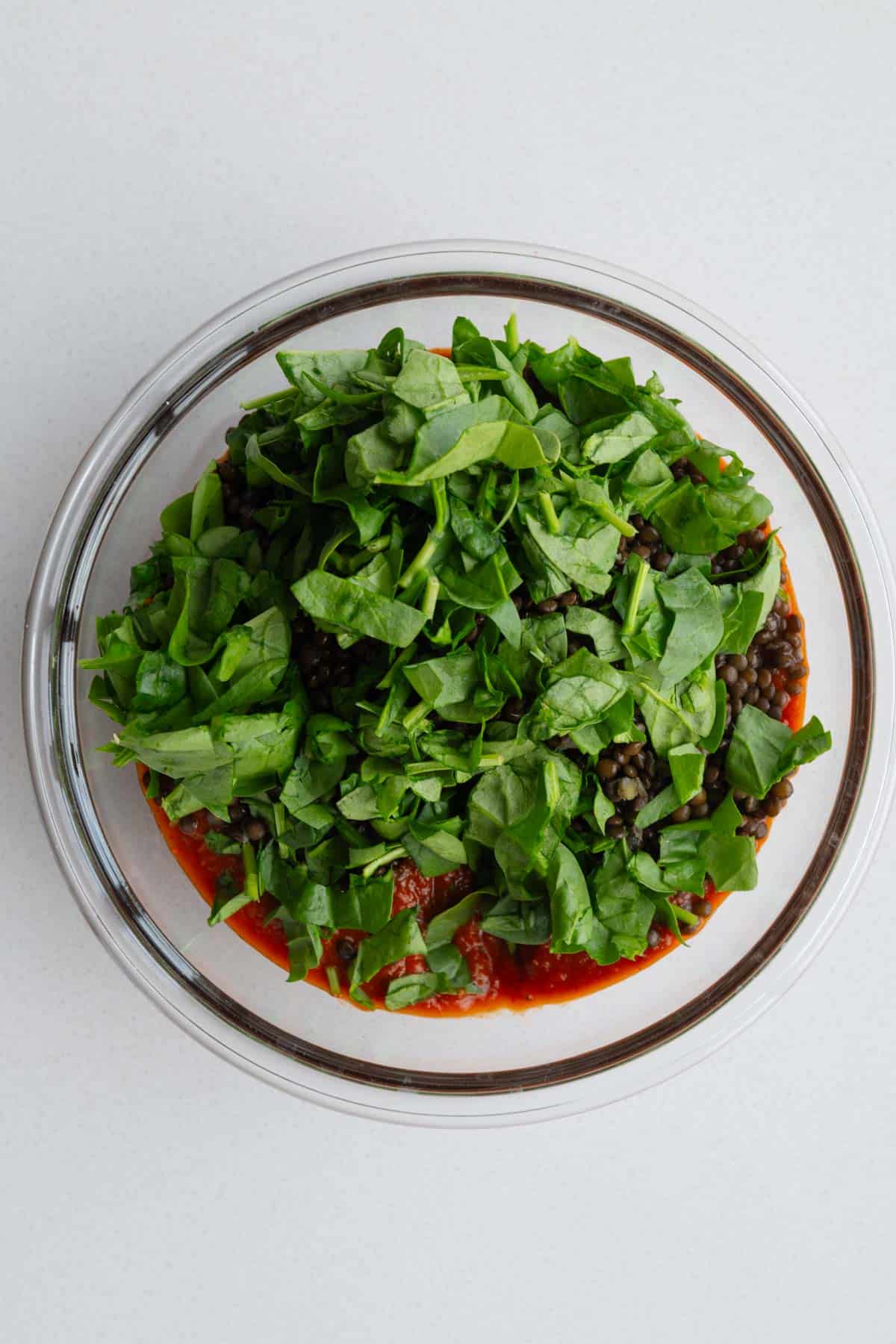 Marinara sauce, cooked lentils, and chopped baby spinach in a bowl.