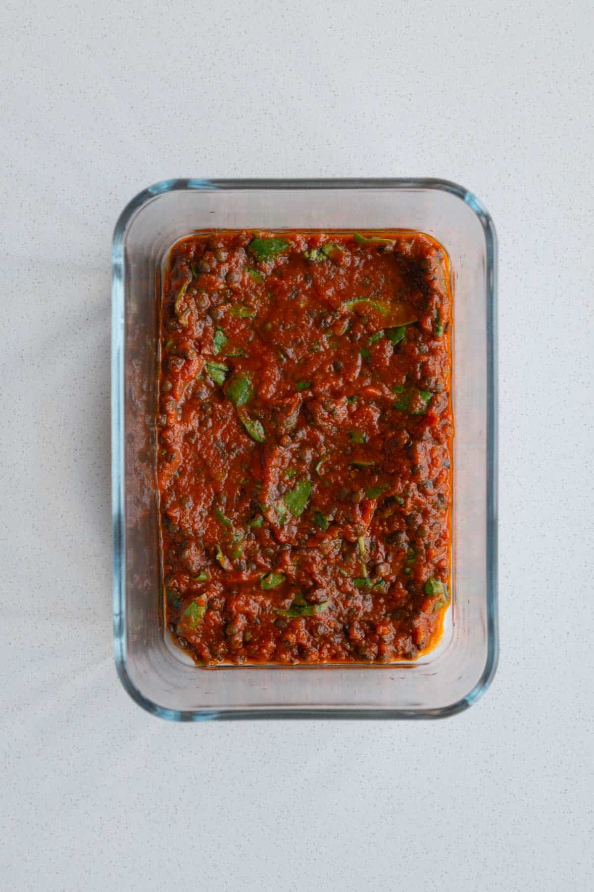 Marinara sauce with lentils and spinach at the bottom of a baking dish.