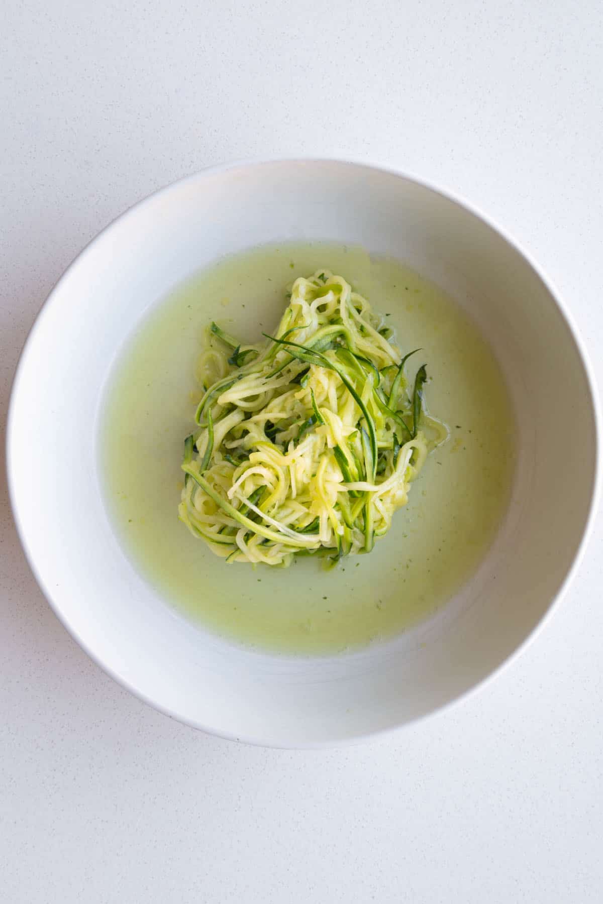 Salted julienned zucchini in a white bowl with water squeezed out.