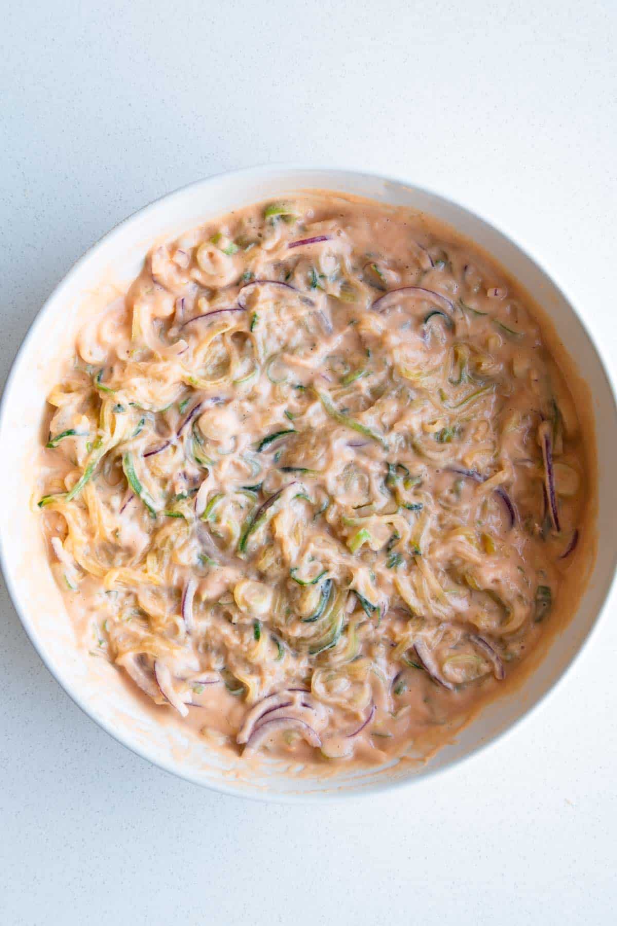 Red lentil batter in a bowl mixed with chopped scallions, julienned zucchini, and sliced red onion.