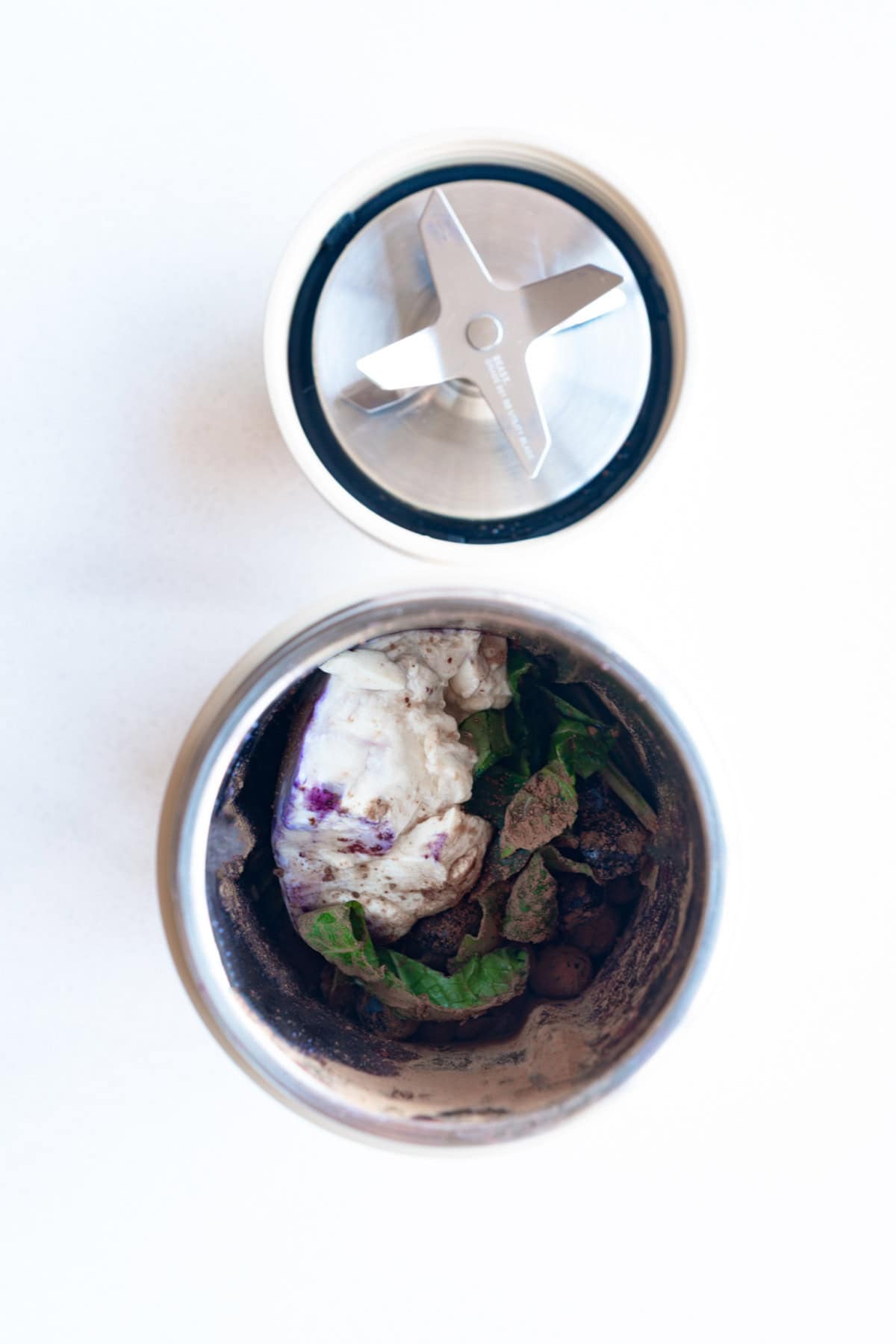Frozen organic blueberries, natural cocoa powder, pumpkin seeds, silken tofu, low-oxalate greens, Medjool date, cinnamon, vanilla, nondairy milk, and ice cubes in a blender.