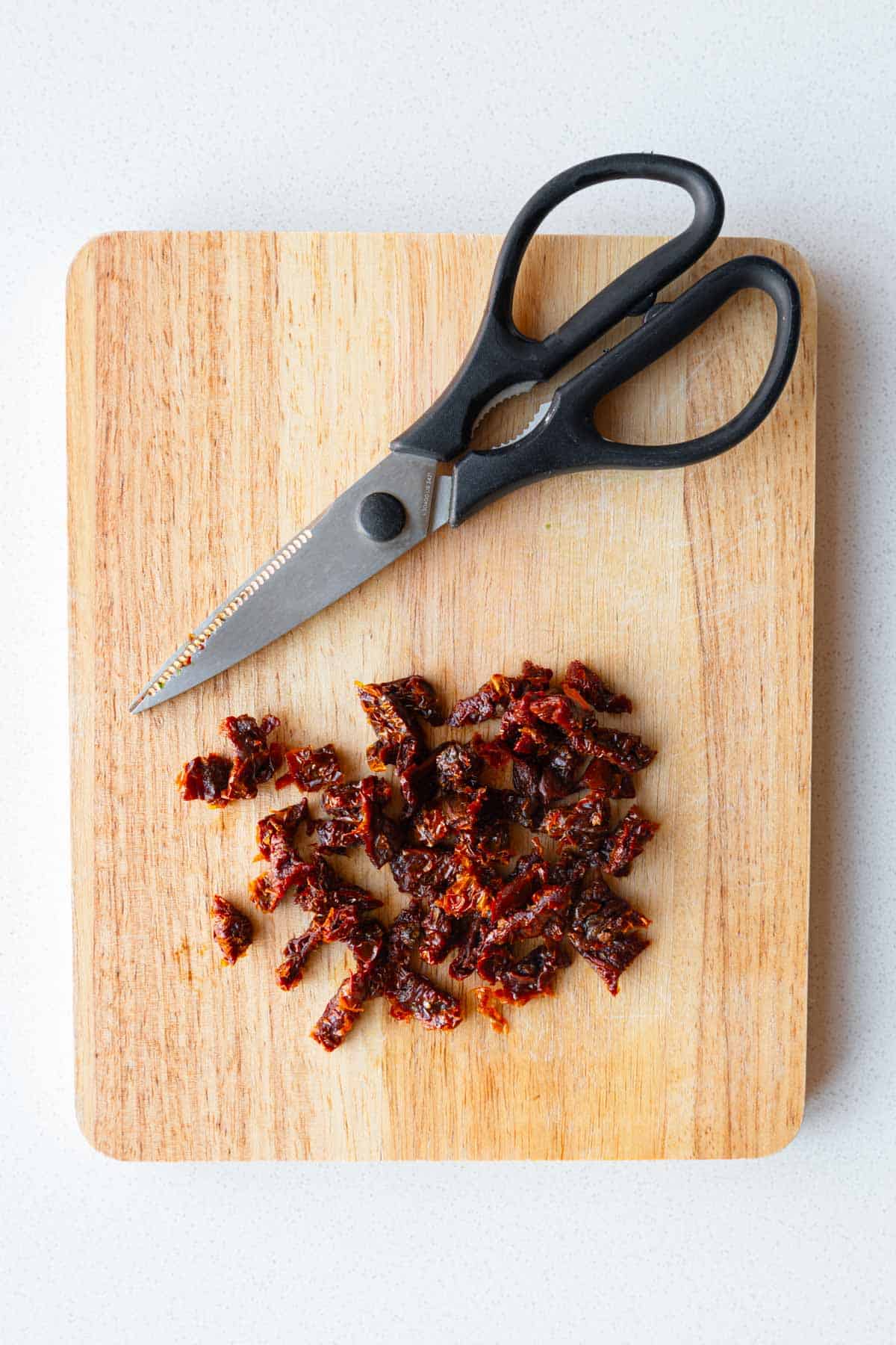 Chopped sun-dried tomatoes on a wooden cutting board.