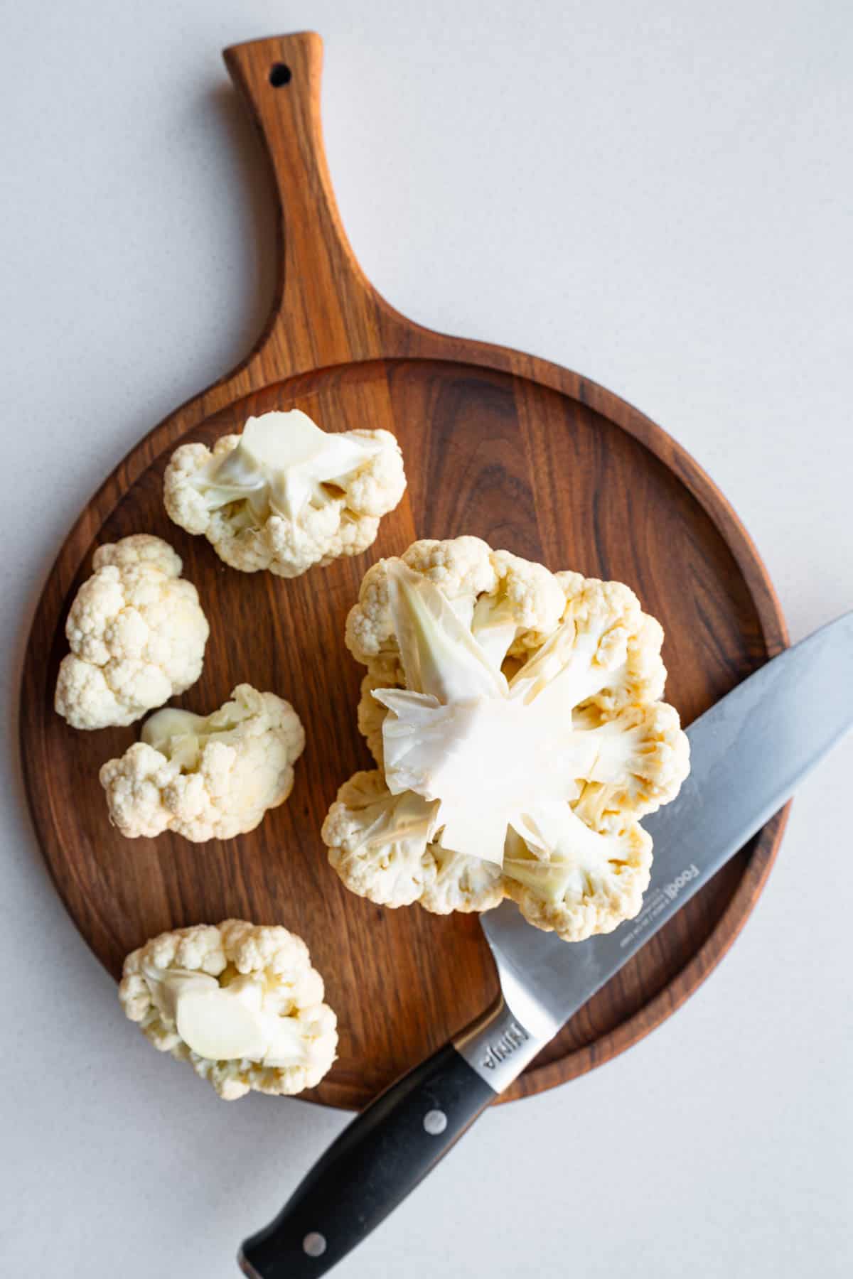 Cut cauliflower florets on a wooden cutting board with a sharp knife.