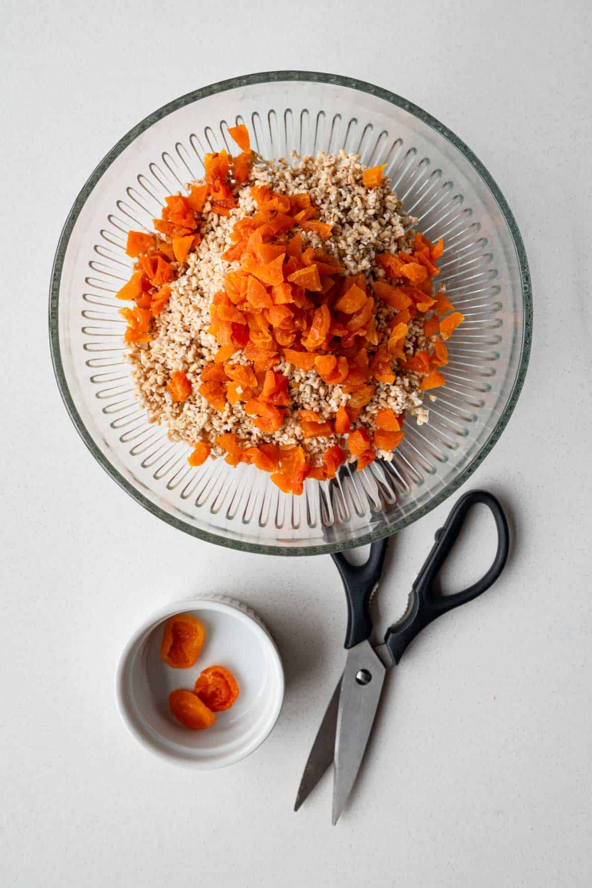Soaked steel-cut oats and chopped dried apricots in a glass bowl next to kitchen shears.
