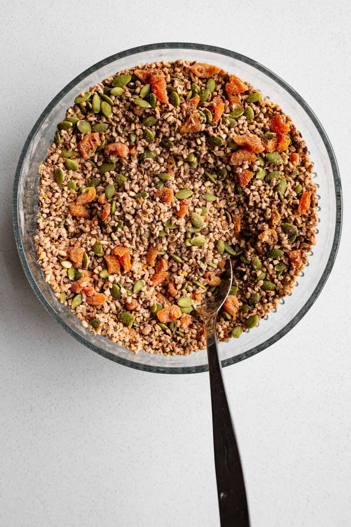 Chopped dried apricot, soaked steel-cut oats, pumpkin seeds, flaxseeds, teff flour, psyllium husk, cinnamon, and orange zest mixed in a glass bowl.