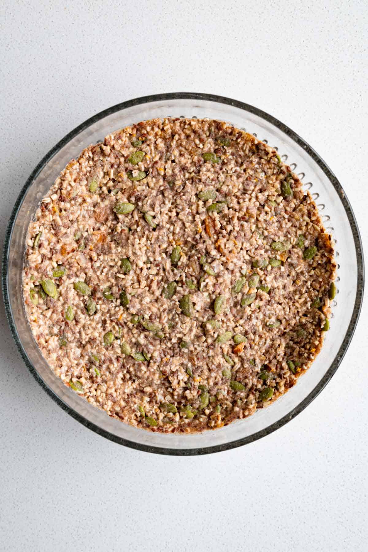 Chopped dried apricot, soaked steel-cut oats, pumpkin seeds, flaxseeds, teff flour, psyllium husk, cinnamon, orange zest , water and apple cider vinegar mixed in a glass bowl.