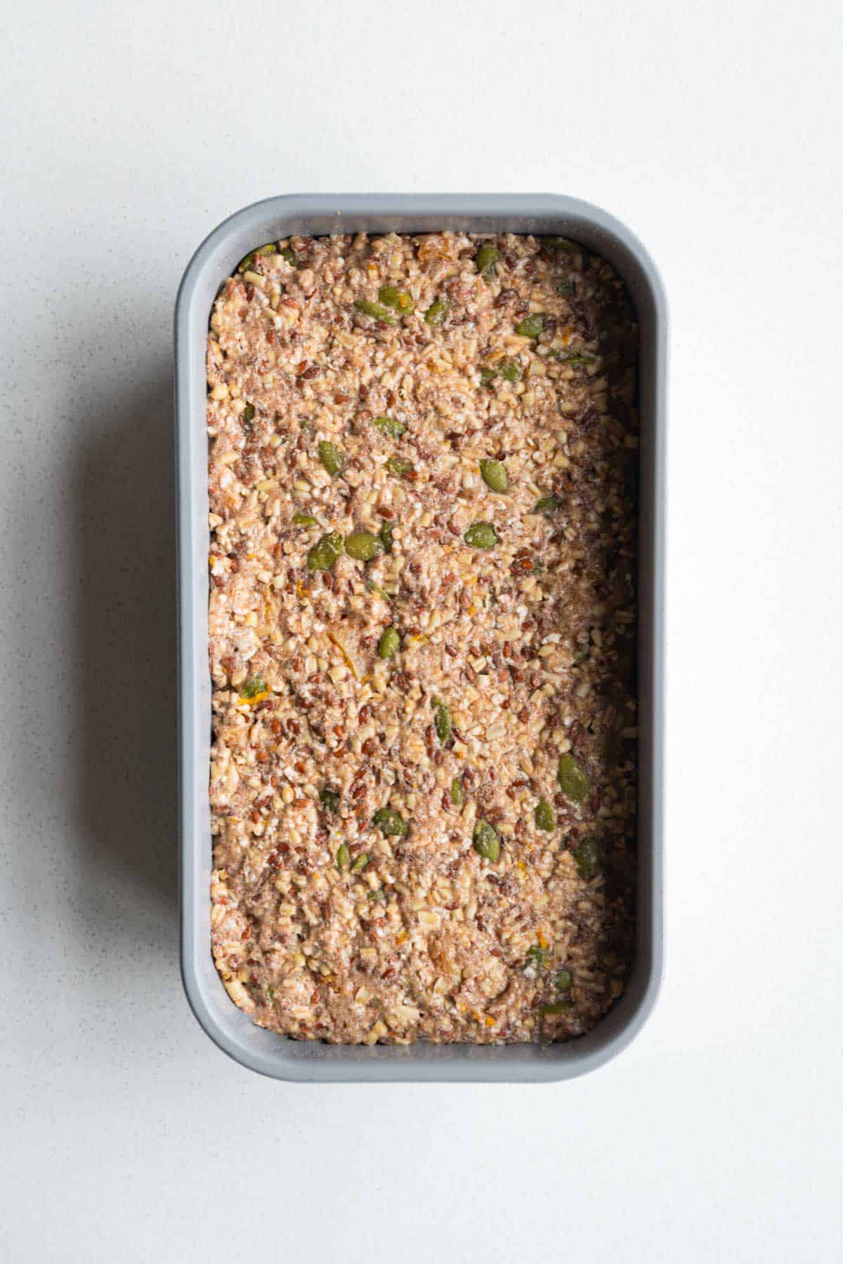Gluten-free oat bread with seeds and dried fruit mixture in a loaf pan.