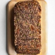 Gluten-free oat bread with seeds and dried fruit sliced on a cutting board.