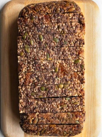 Gluten-free oat bread with seeds and dried fruit sliced on a cutting board.