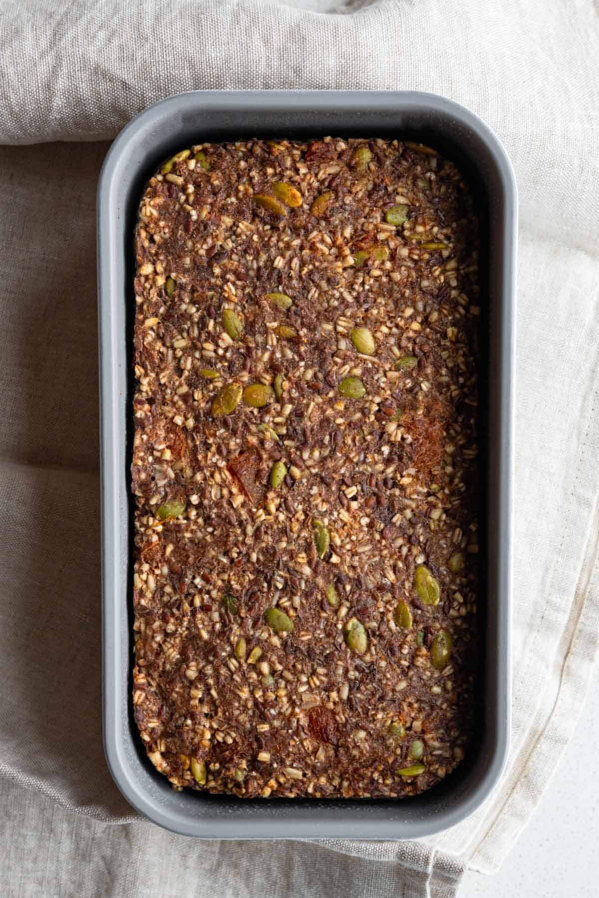 Gluten-free oat bread with seeds and dried fruit in a loaf pan.