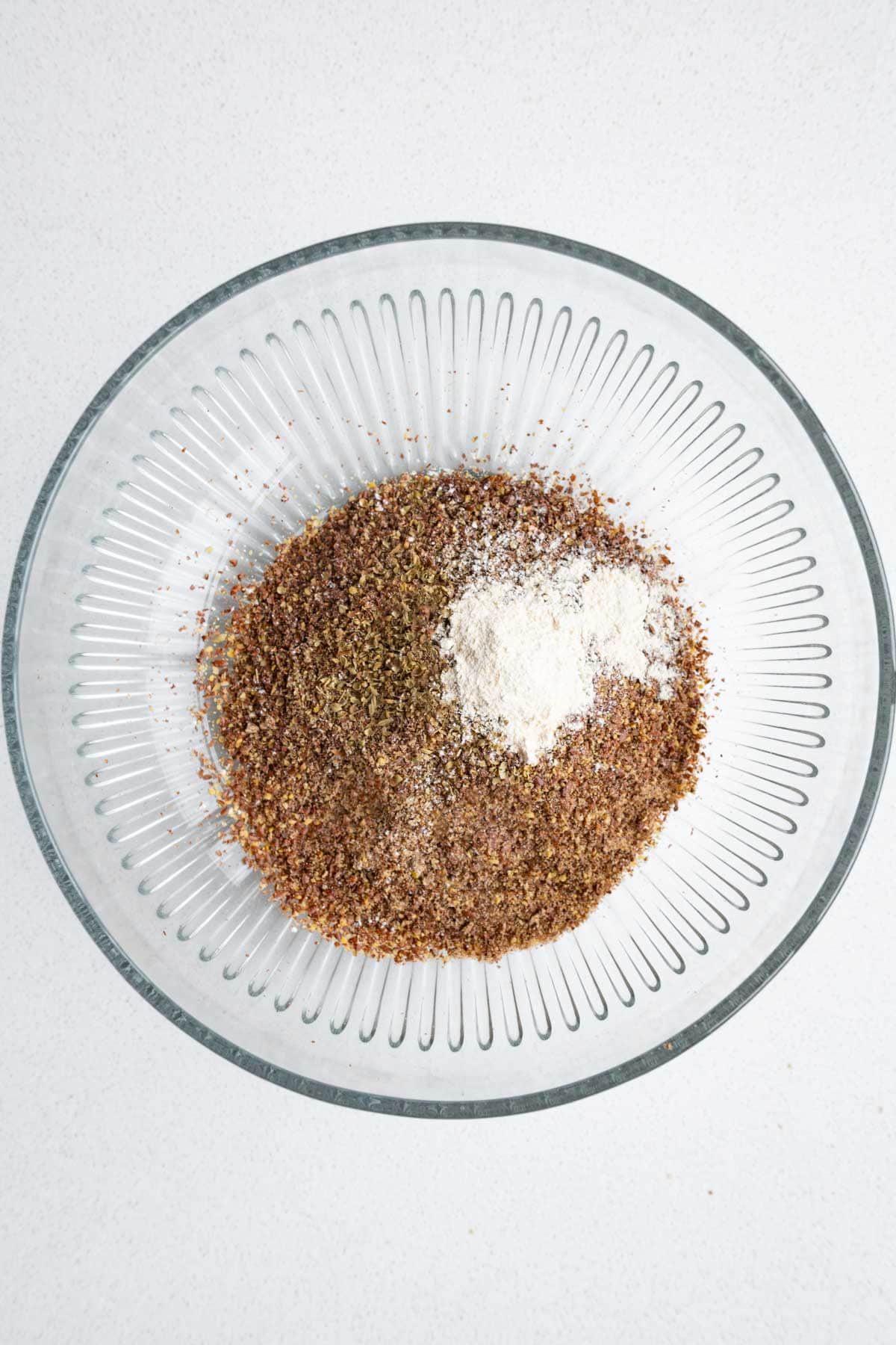 Ground flaxseeds, garlic powder, and dried herbs in a glass bowl.