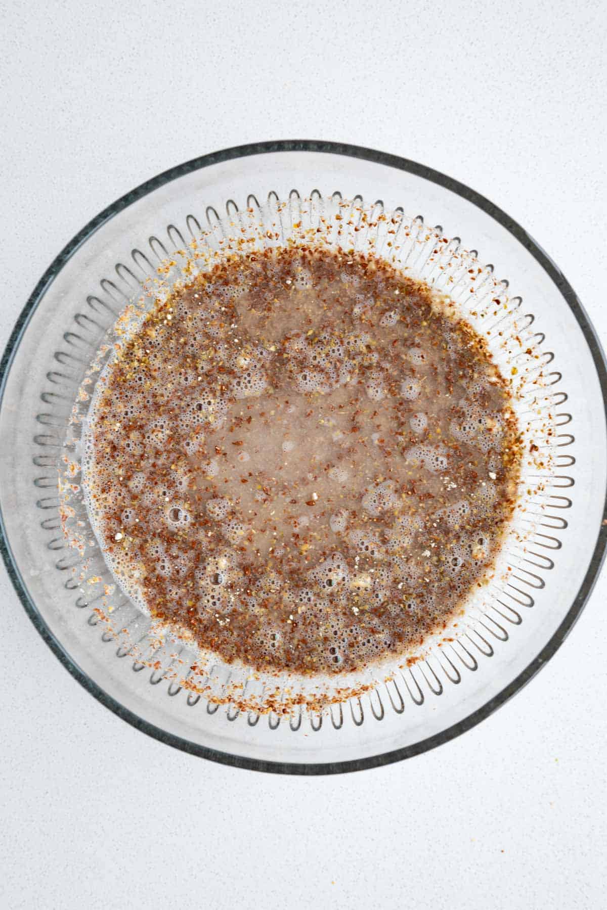 Ground flaxseeds, garlic powder, dried herbs, and water in a glass bowl.