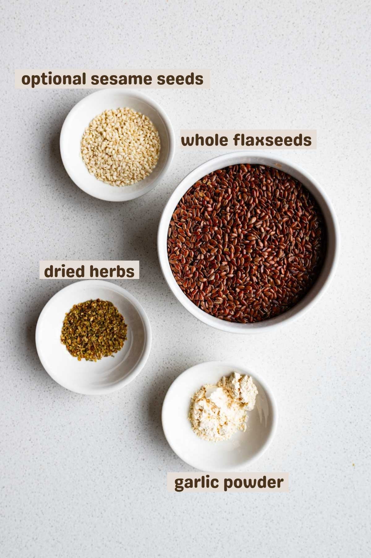 Whole flaxseeds, garlic powder, dried herbs, and sesame seeds.
