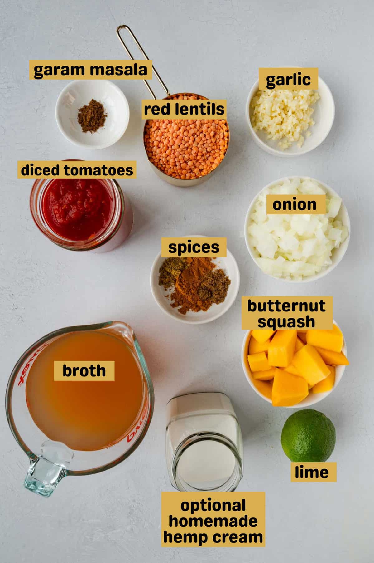 Red lentils, garam masala, broth, cubed butternut squash, coconut milk, lime, spices, diced onion, minced garlic, and diced tomatoes on a gray backdrop.