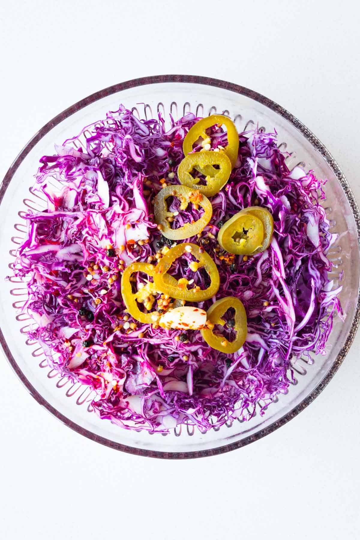Shredded red cabbage, lime juice, garlic, coriander seeds, black peppercorns, crushed red pepper, water, and apple cider vinegar in a bowl.