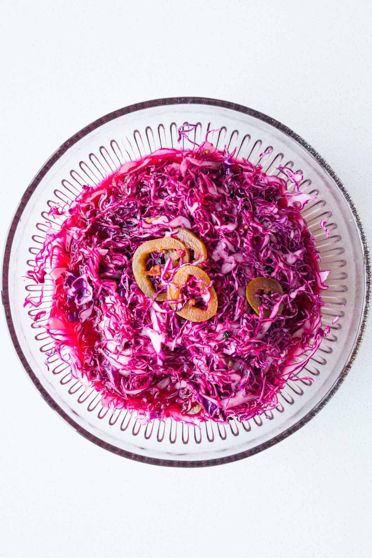 Shredded red cabbage, lime juice, garlic, coriander seeds, black peppercorns, crushed red pepper, water, and apple cider vinegar tossed in a bowl.