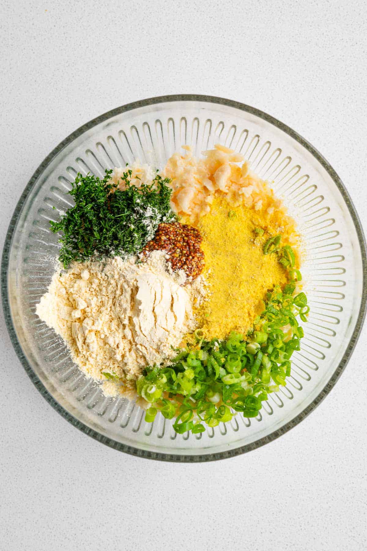 Chopped green onion, dill, chickpea flour, mashed white beans, garlic and onion powder, nutritional yeast and mustard in a bowl.