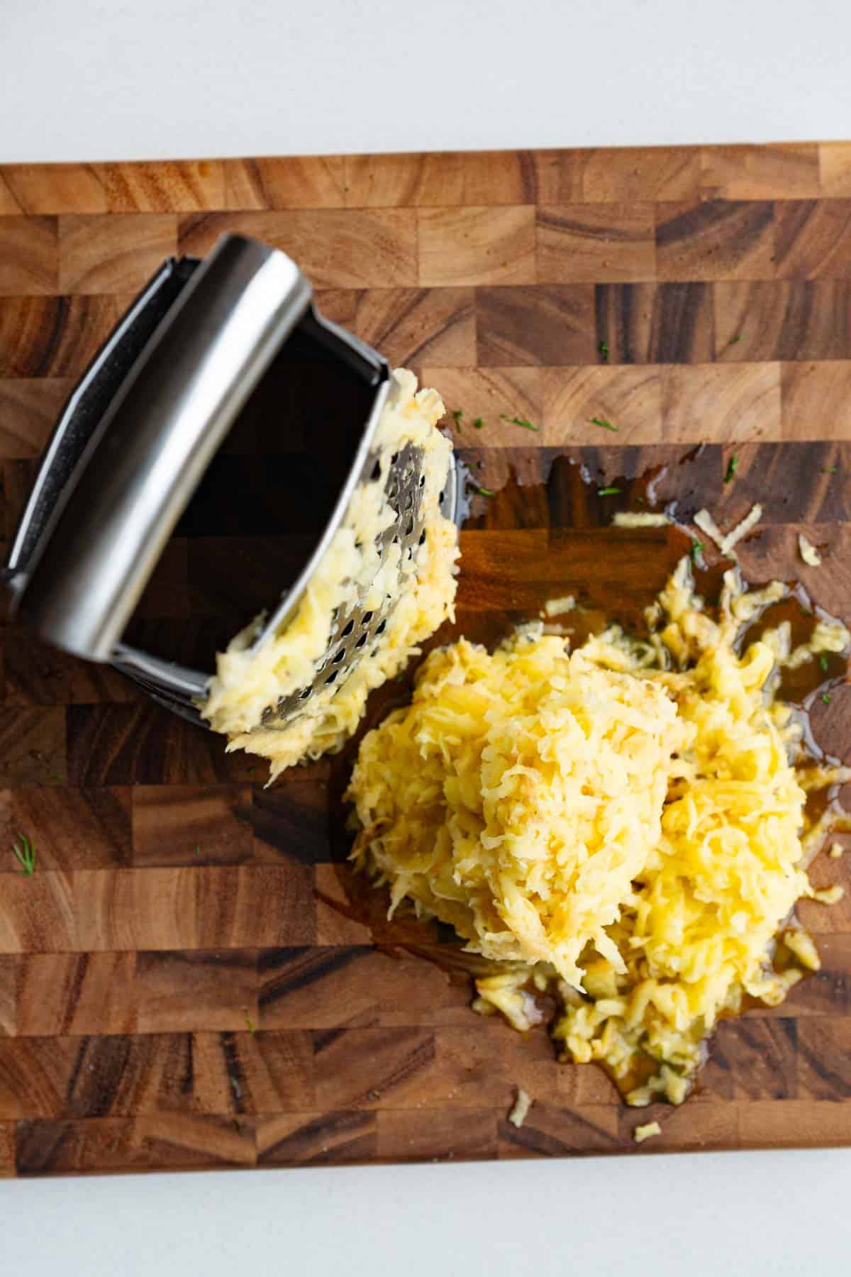 Grated potatoes and a box grater on a wooden cutting board.