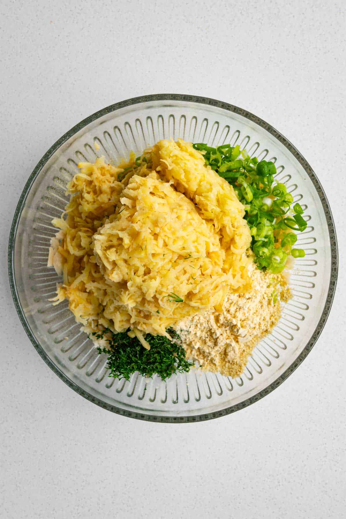 Grated Yukon Gold potatoes, chopped green onion, dill, chickpea flour, mashed white beans, garlic and onion powder, nutritional yeast and mustard in a bowl.