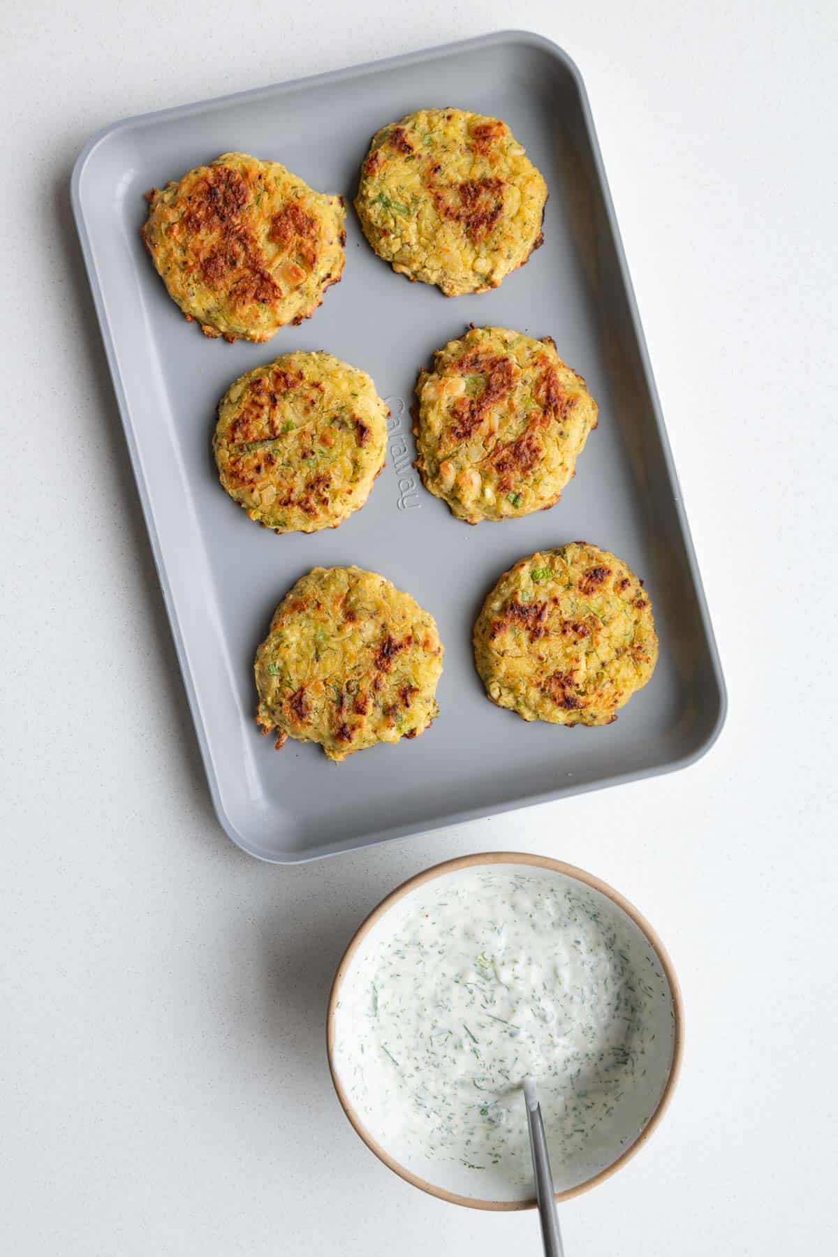 Baked potato fritters on a baking sheet with vegan tzatziki sauce.