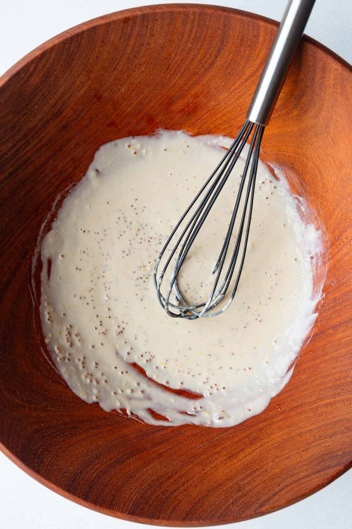 Whisked creamy tahini dressing in a wooden bowl.