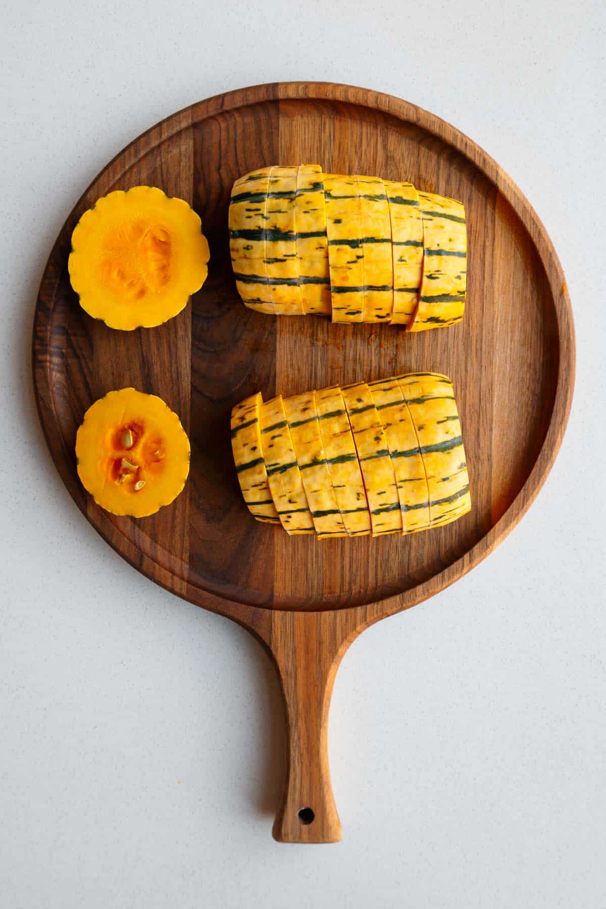 Sliced delicata squash on a wooden cutting board.
