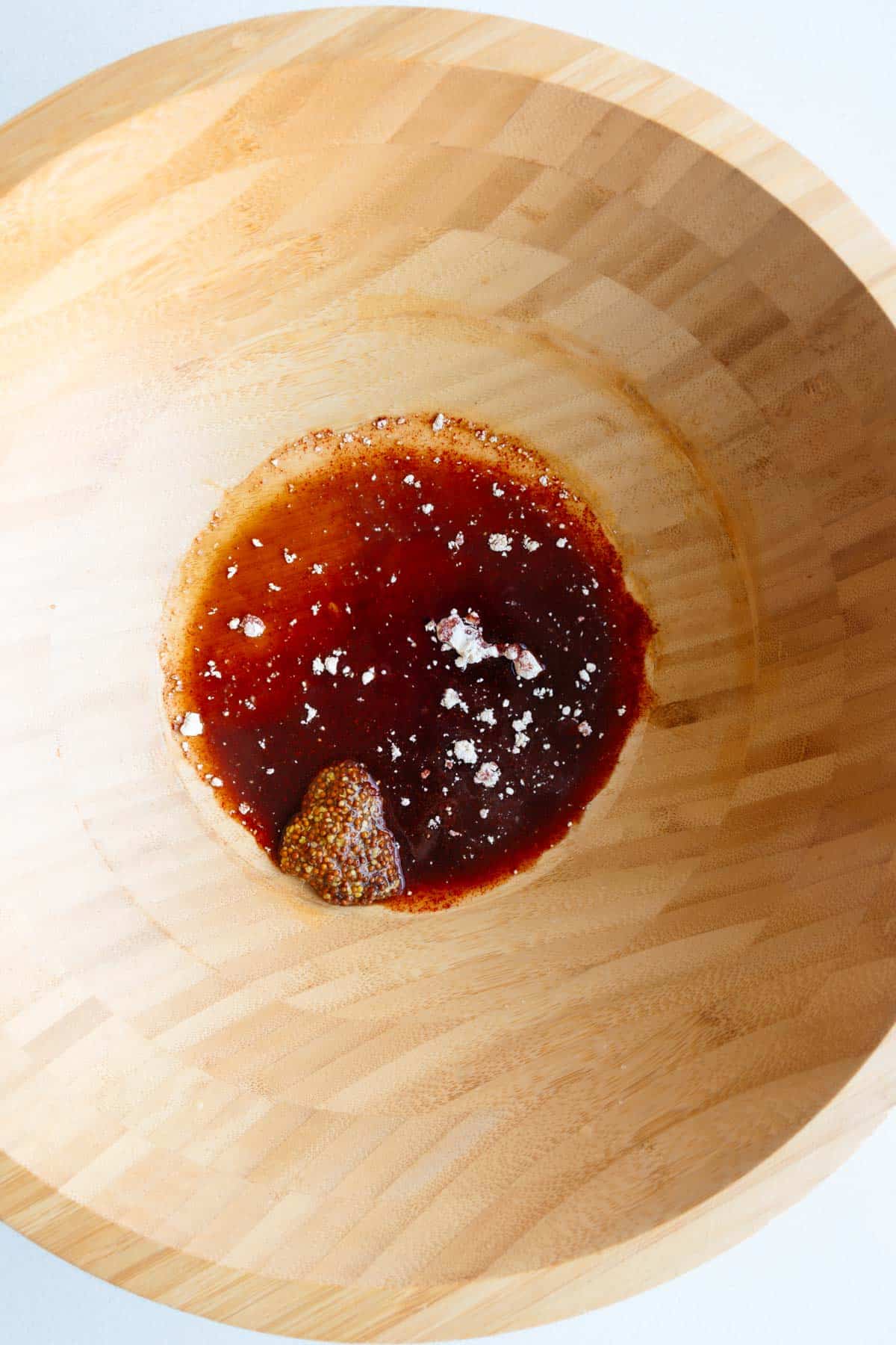 Balsamic vinegar, lemon juice, Dijon or stone-ground mustard, maple syrup, garlic powder, smoked paprika in a wooden bowl.