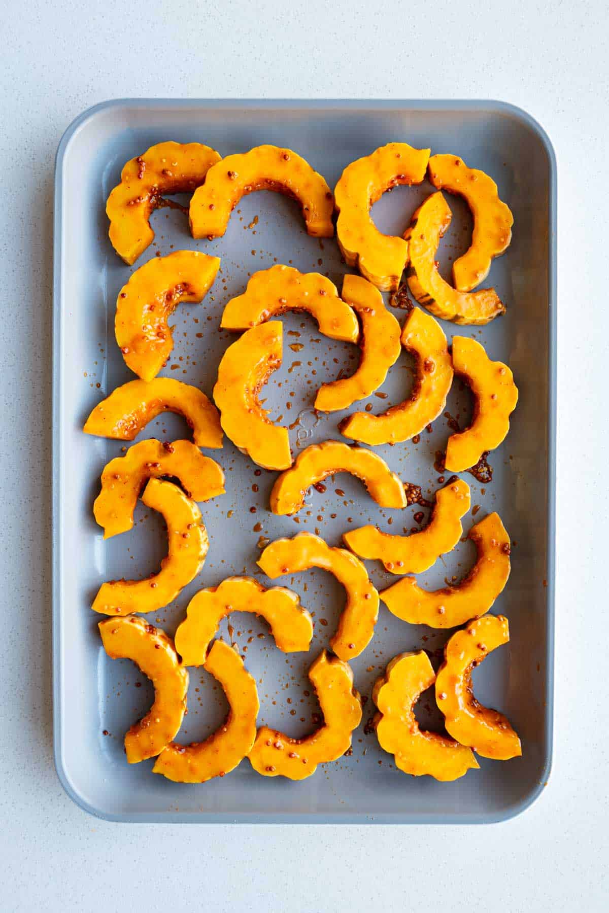 Delicata squash sliced and marinated on a baking sheet.