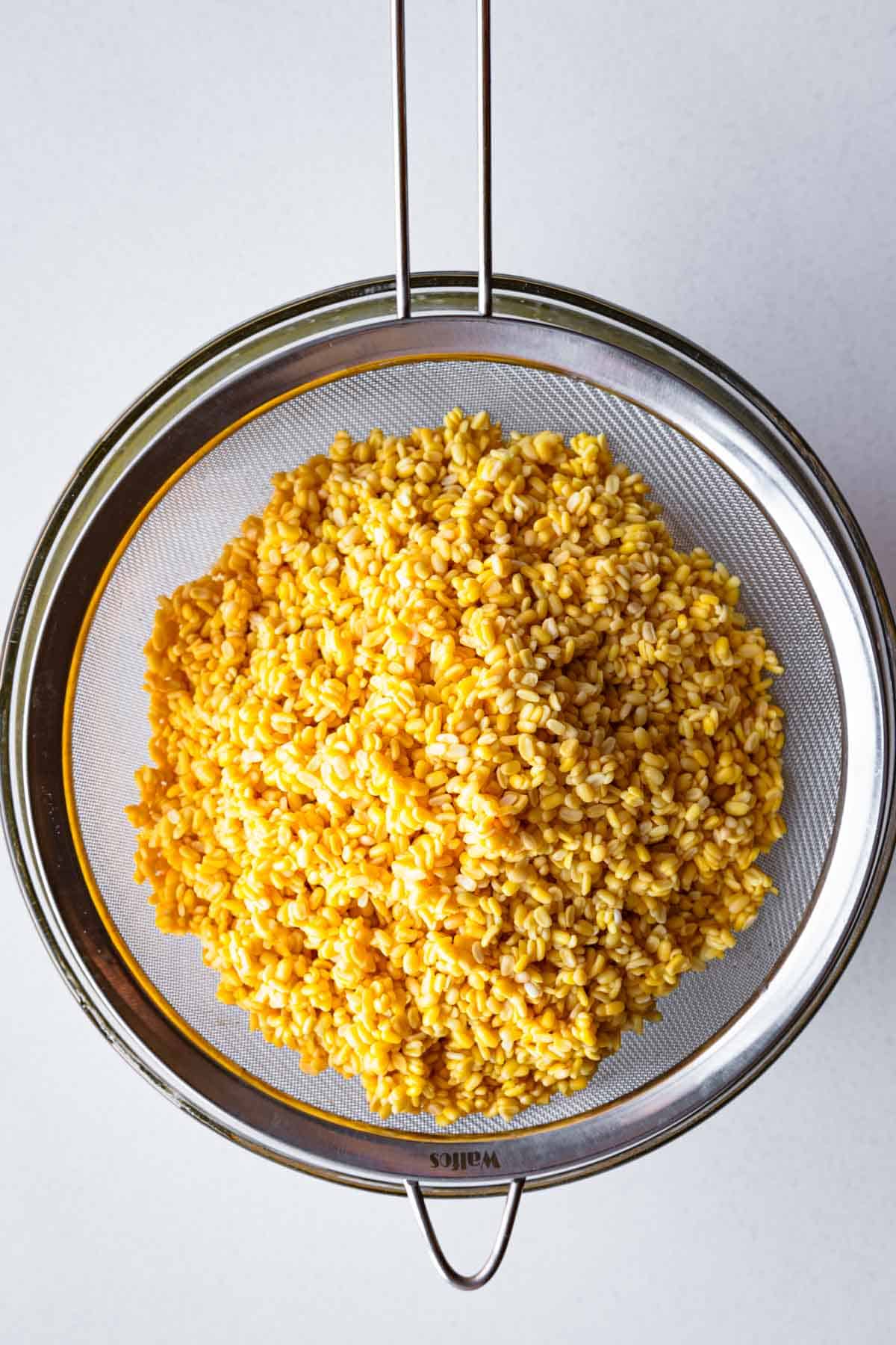 Drained soaked mung beans (moong dal) in a fine mesh sieve.