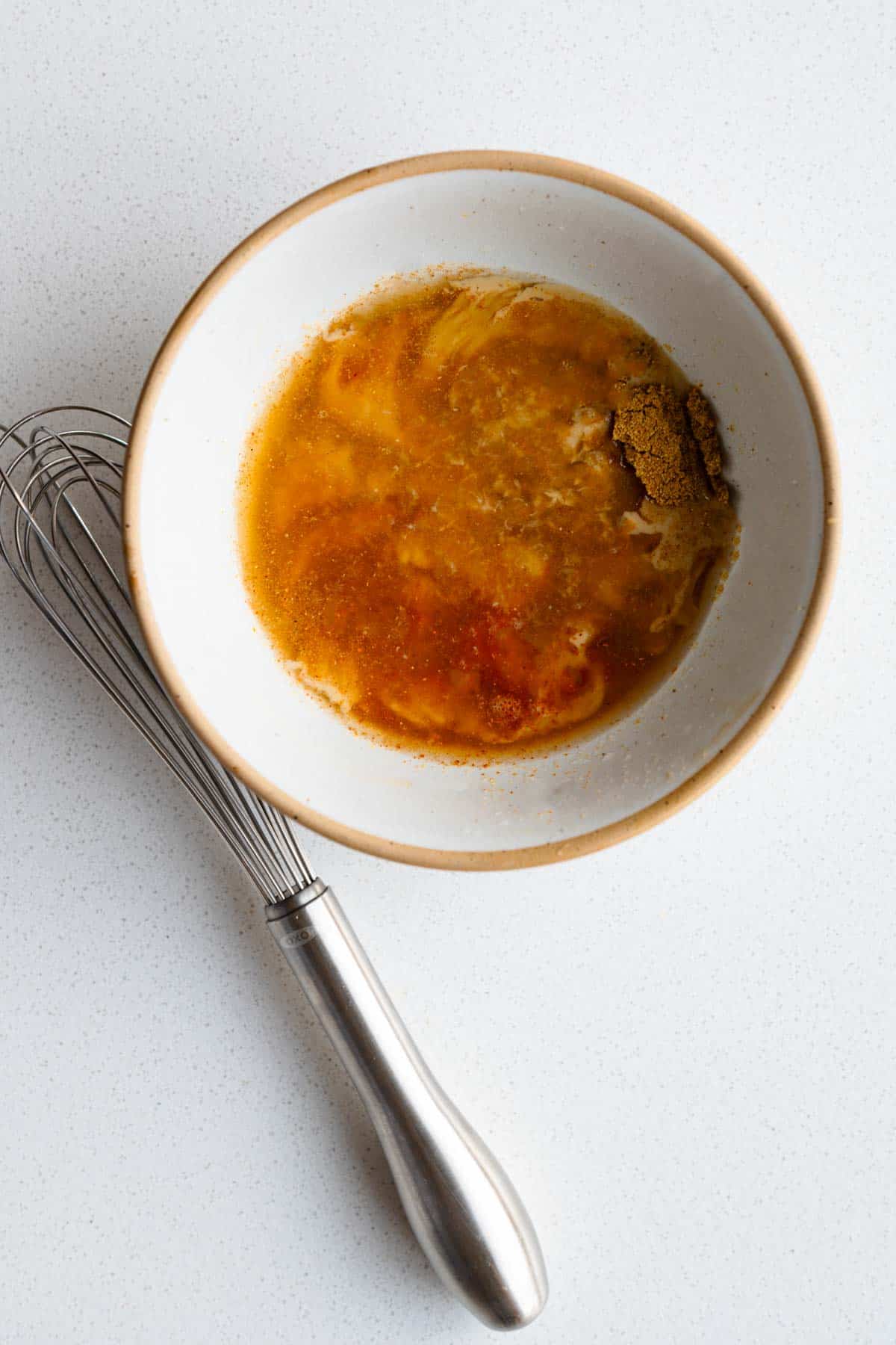 Tahini, tamarind puree, maple syrup, cumin, coriander, cayenne, lime juice and water in a bowl next to a whisk.