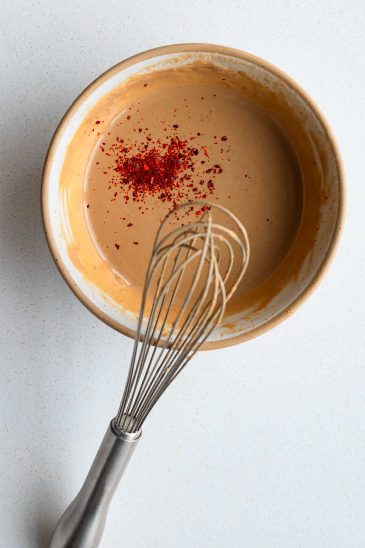 Tamarind dressing in a bowl with a whisk topped with red chili powder.