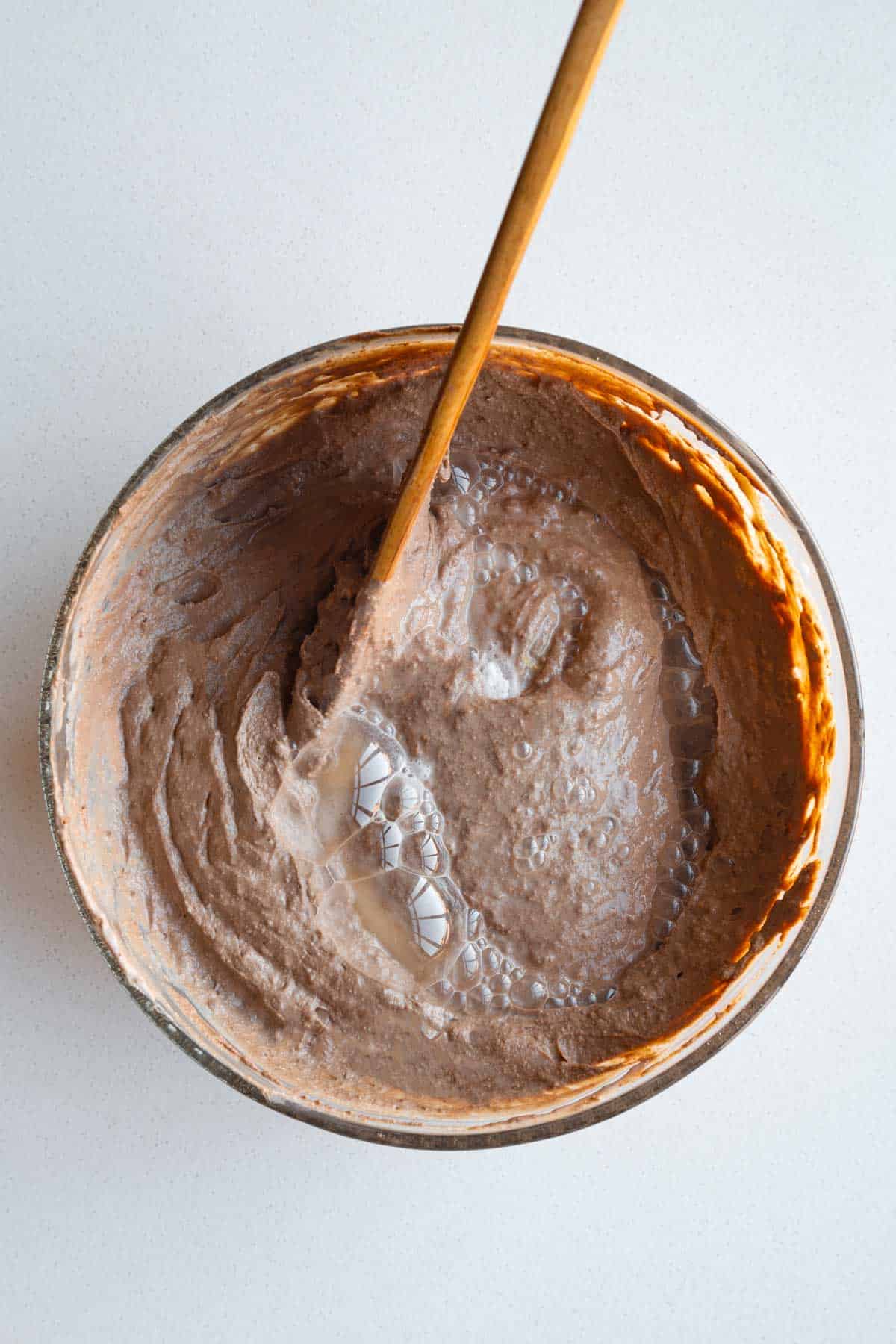 Batter for Vegan Banana Bread Tofu Brownies in a glass bowl with baking soda and apple cider vinegar.