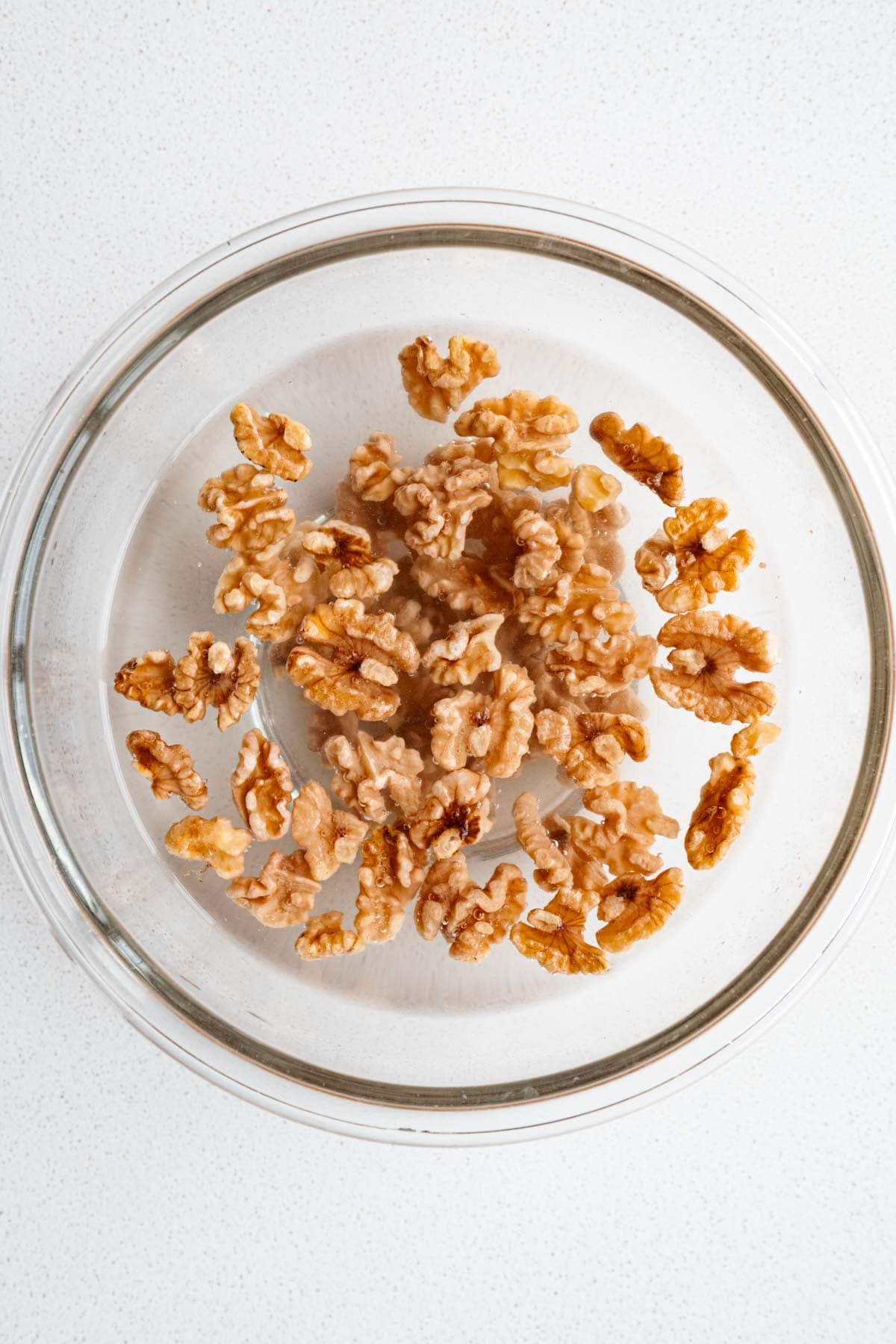 Walnuts soaking in hot water in a glass bowl.